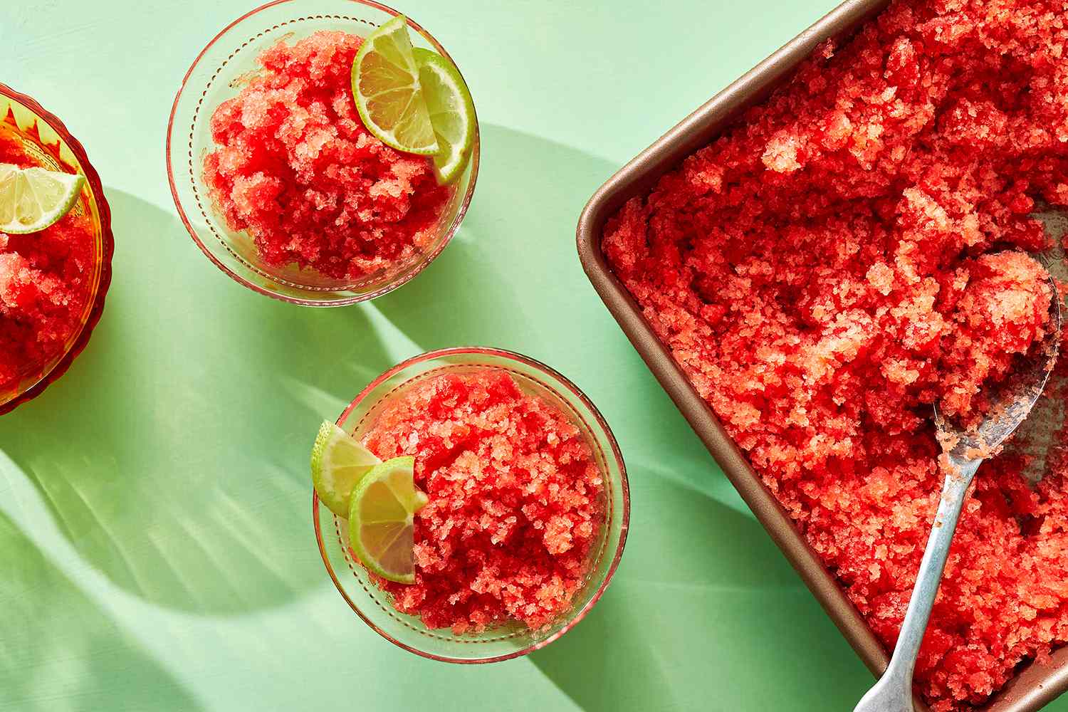A bowl of bright pink watermelon granita with a lime wedge on the side