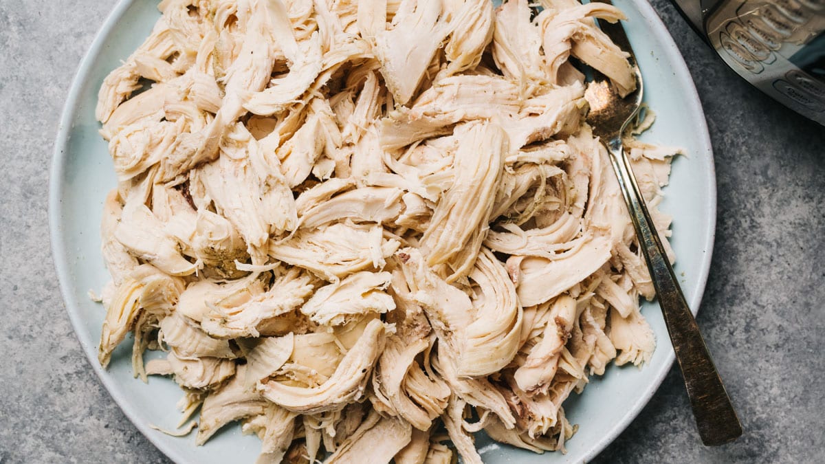 A bowl of shredded rotisserie chicken on a kitchen counter with tortillas and shredded cheese nearby