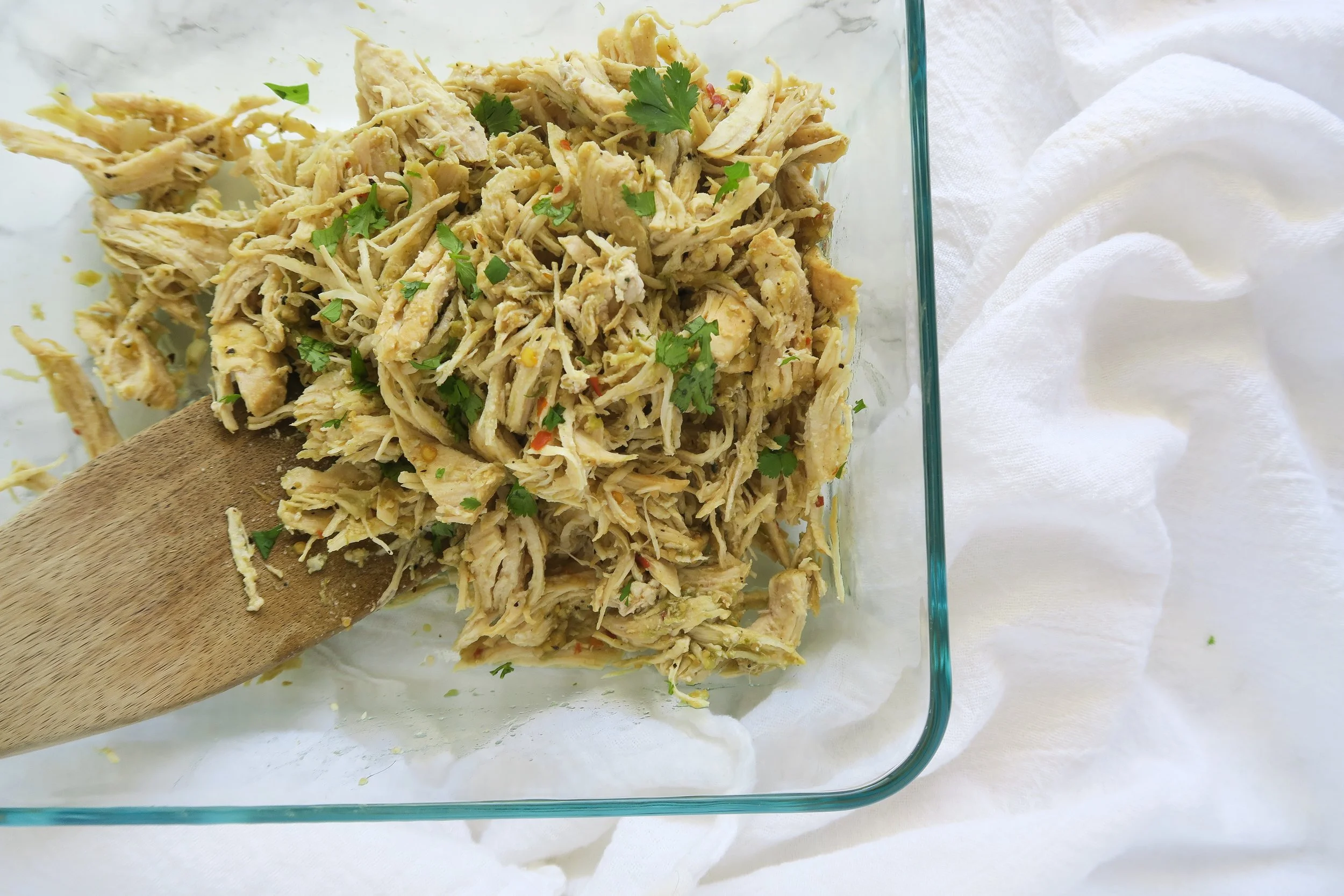 A family-style taco bar with bowls of shredded salsa verde chicken, chopped cilantro, diced onions, shredded cabbage, cheese, and warm tortillas