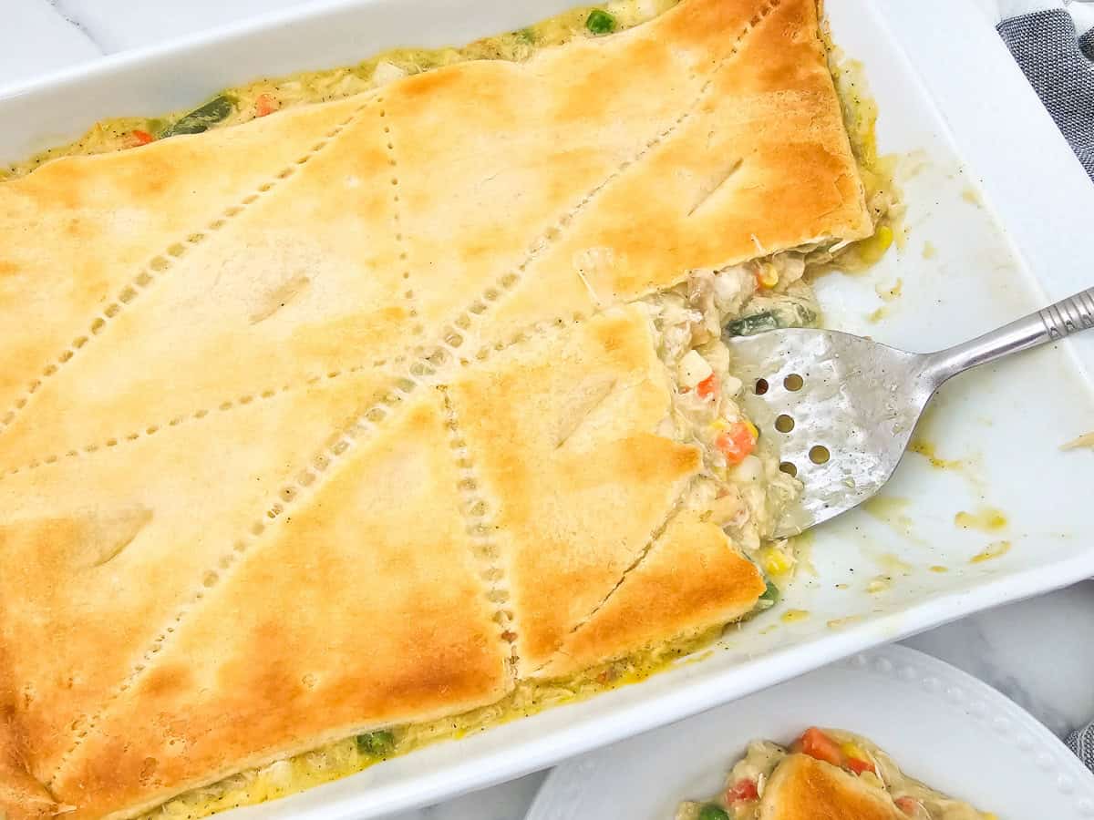 A freshly baked chicken pot pie on a rimmed sheet pan with puff pastry browned and flaky, with bubbling creamy filling visible at the edges