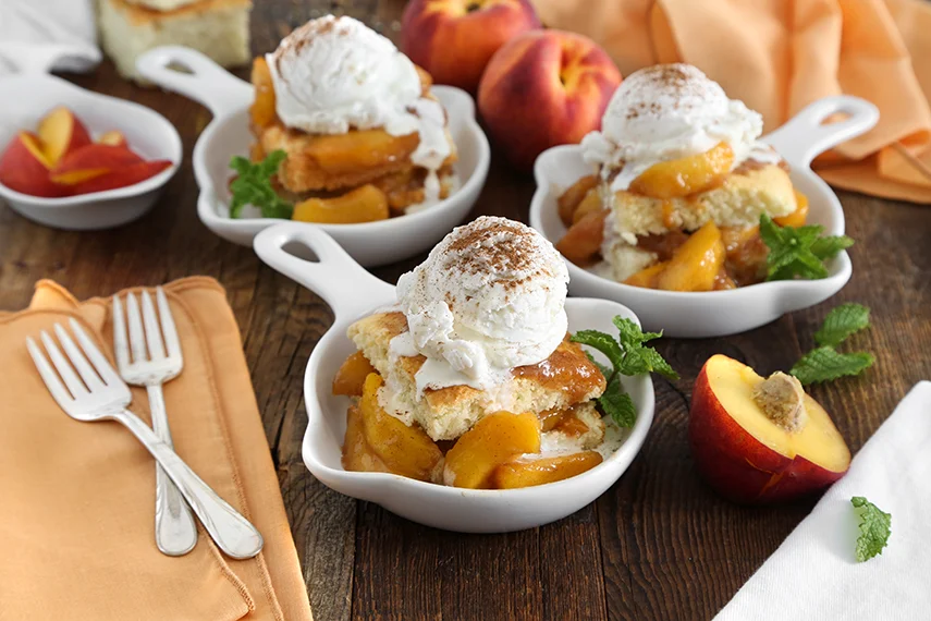 A glass dessert cup layered with cubes of pound cake, juicy peaches, and a swirl of whipped cream