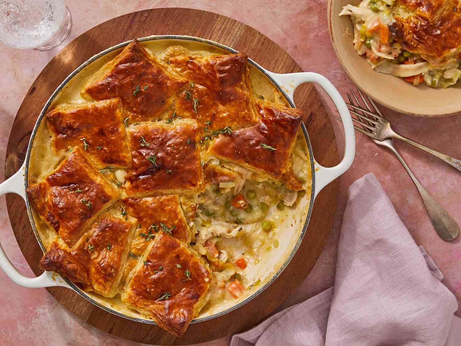 A golden baked chicken pot pie in a ceramic baking dish with puff pastry domed and deeply browned, steam rising as a spoon lifts out creamy chicken and vegetable filling