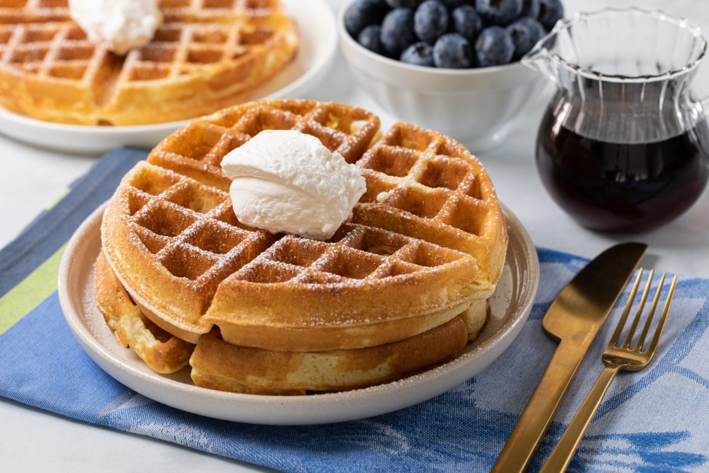 A golden homemade waffle on a ceramic plate with a pat of butter melting on top, morning light on the table