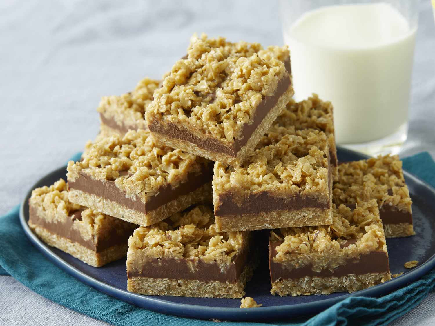A pan of no-bake peanut butter oat bars with a smooth chocolate top, sliced into neat rectangles on parchment paper