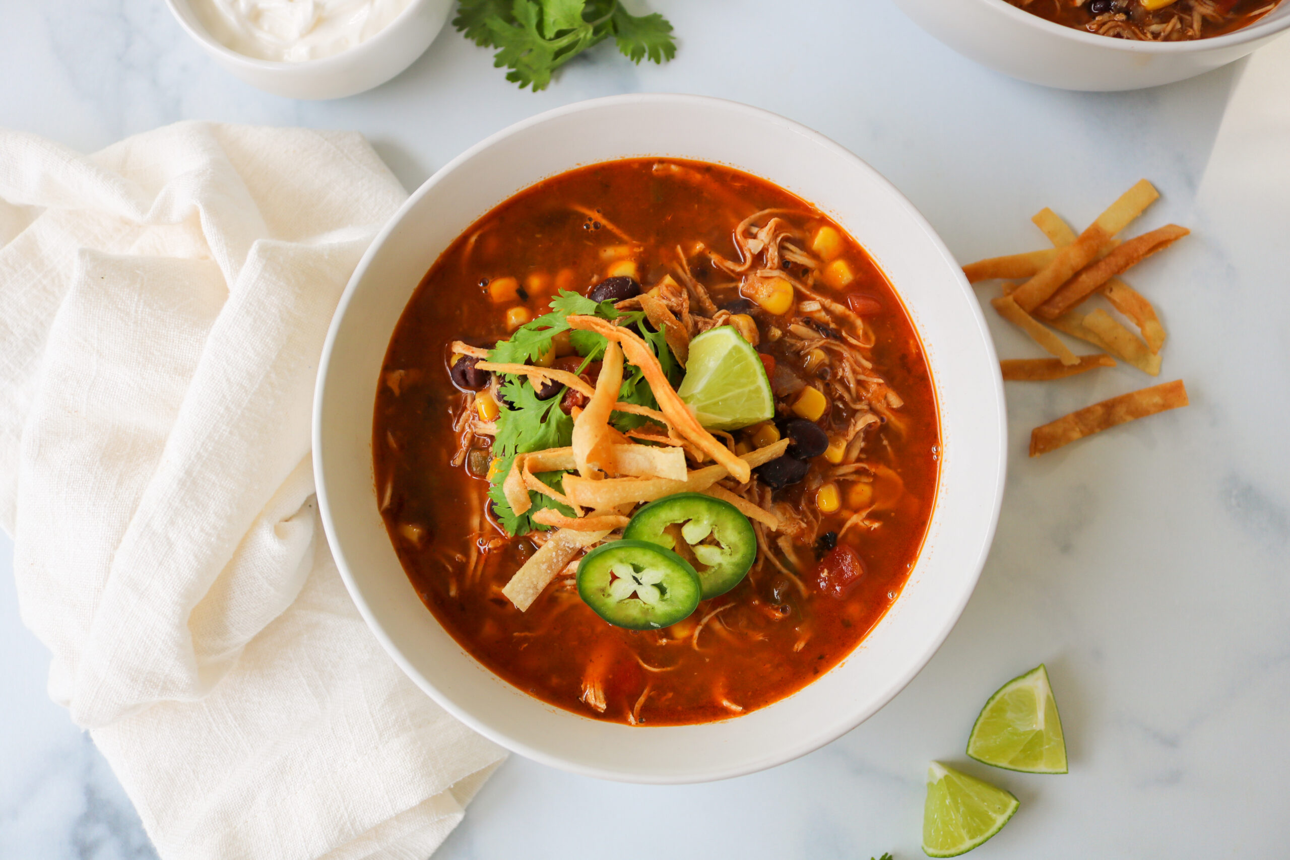 A pot of creamy chicken tortilla soup on the stove with a wooden spoon stirring visible shreds of chicken, black beans, and corn
