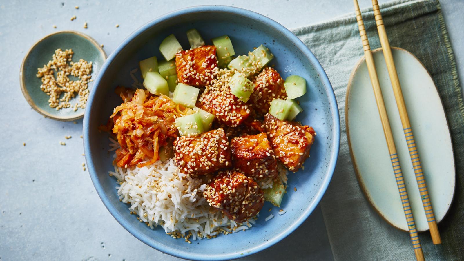 A rice bowl topped with garlic butter salmon bites, sliced cucumber, avocado, and lemon wedges on a wooden table