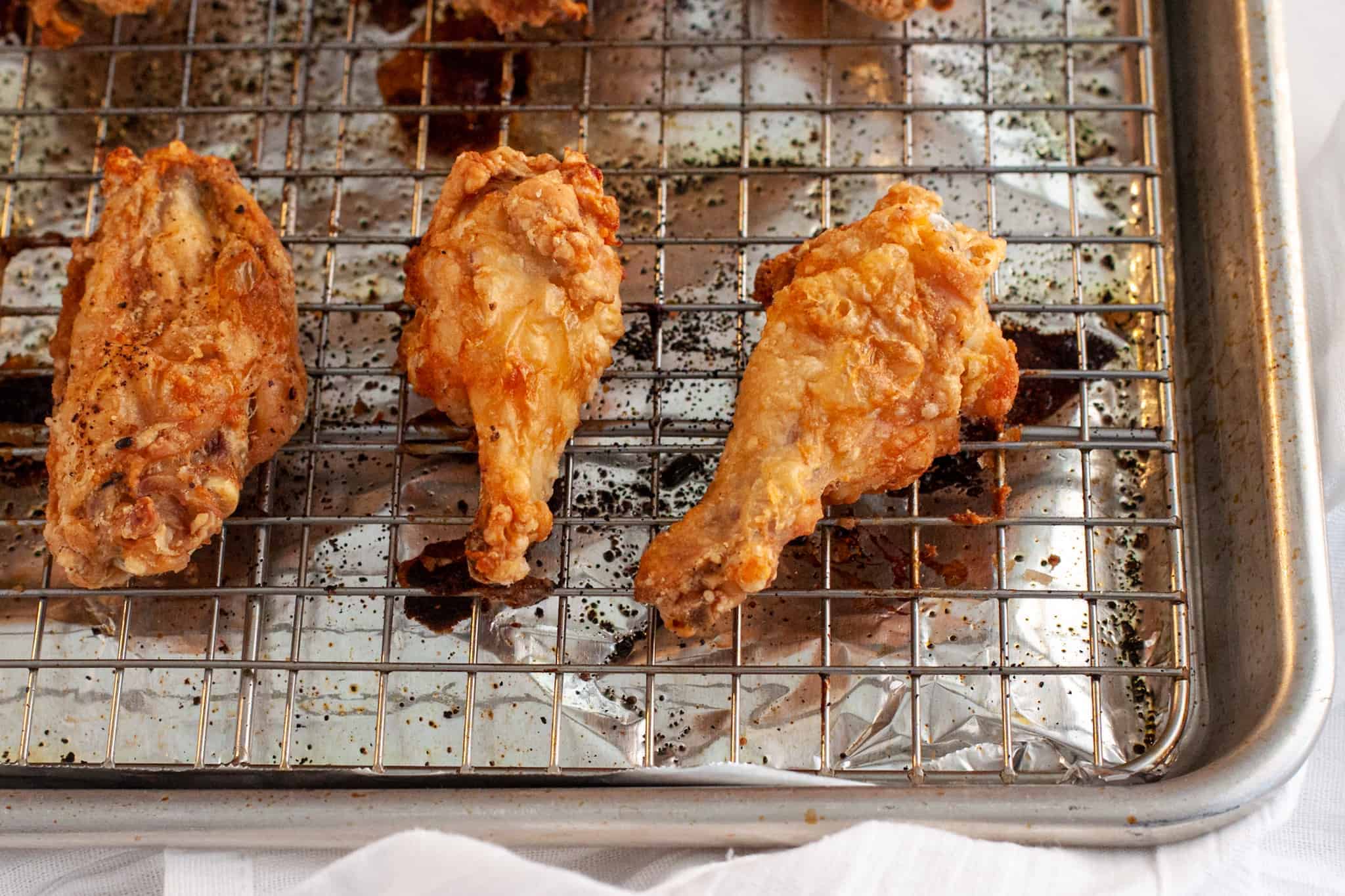 A sheet pan of baked chicken wings under a broiler with skin turning blistered and extra crisp at the edges