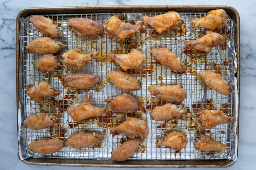 A single layer of golden brown baked chicken wings on a wire rack set over a sheet pan, with crisp blistered skin and rendered fat on the tray