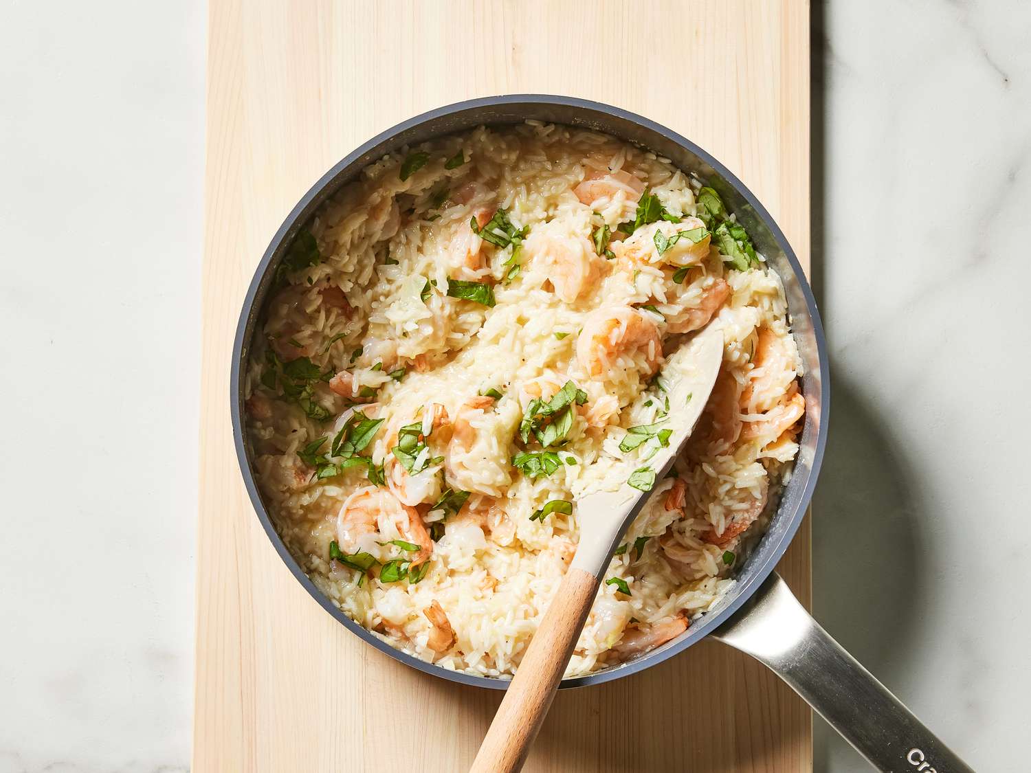 A skillet filled with fluffy rice and pink curled shrimp, topped with chopped parsley and lemon slices on a kitchen counter