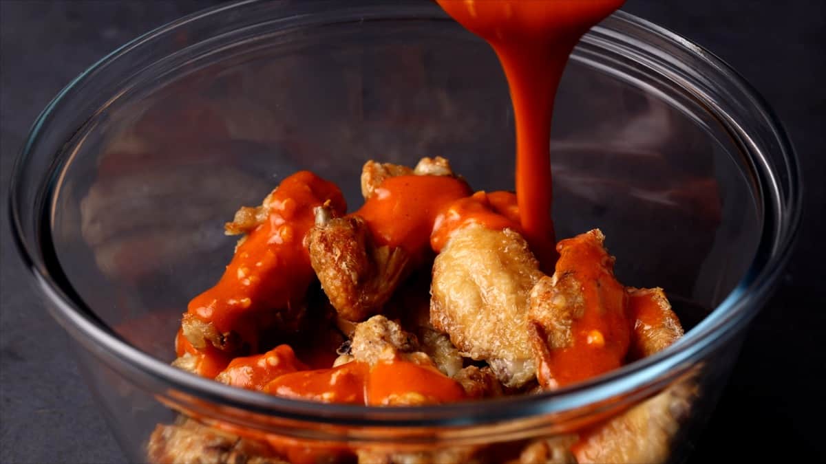 Crispy baked chicken wings piled on a platter with a small bowl of buffalo sauce for dipping