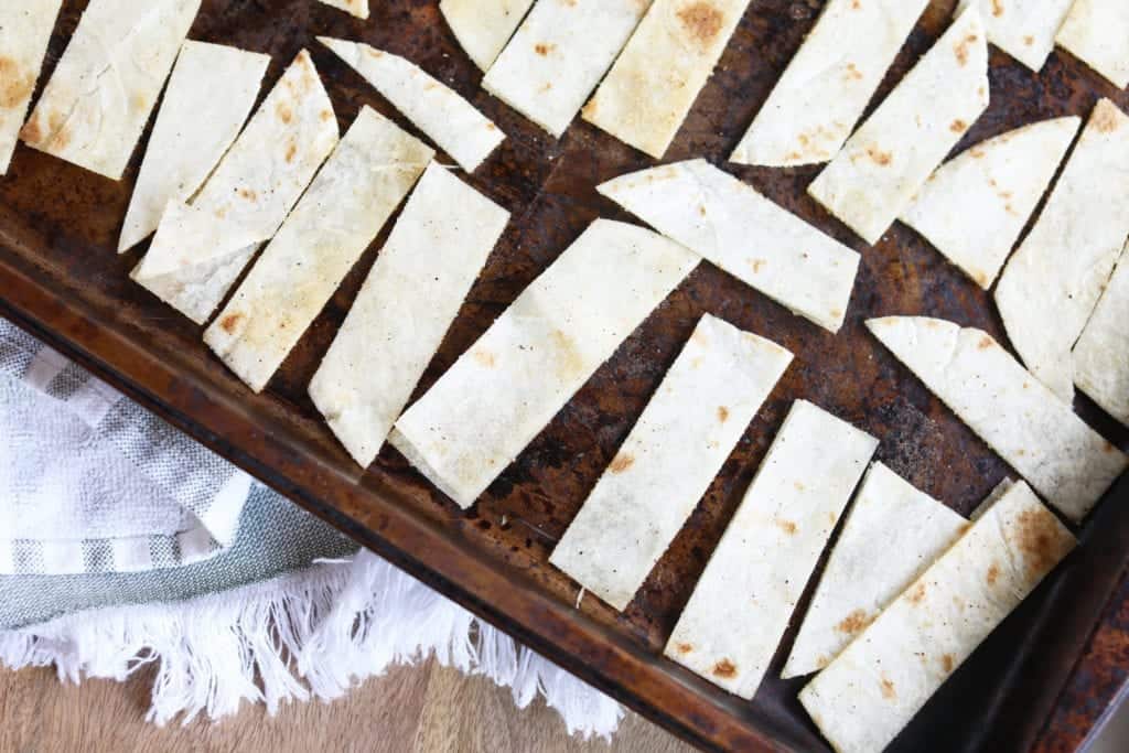 Crispy golden tortilla strips spread on a parchment-lined baking sheet fresh from the oven