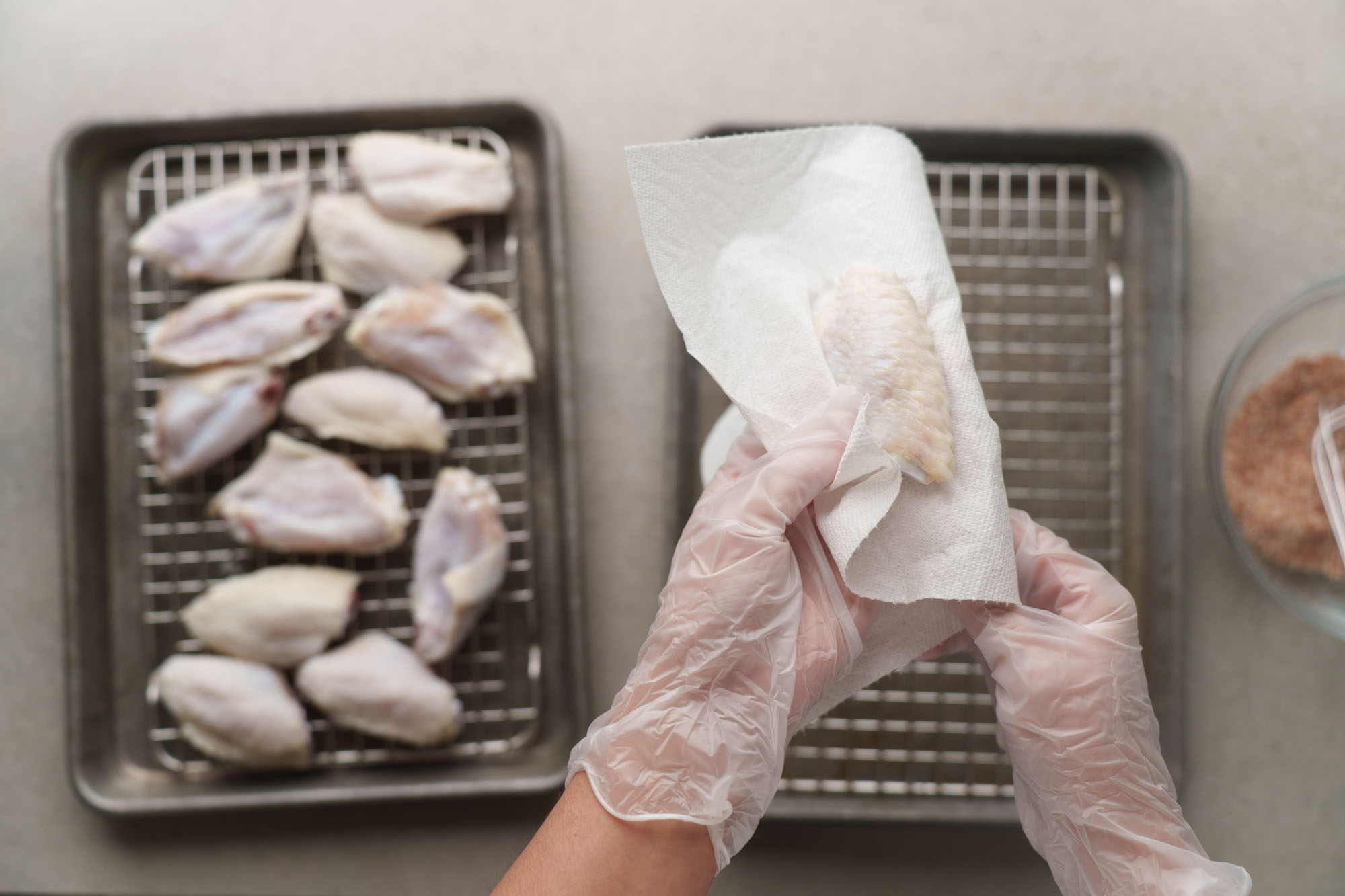 Raw chicken wings being patted very dry with paper towels on a cutting board next to a large mixing bowl