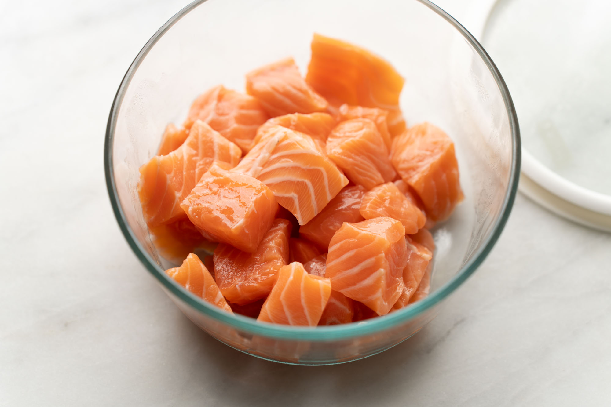 Raw salmon cut into even 1-inch cubes on a cutting board with a chef's knife and a lemon nearby