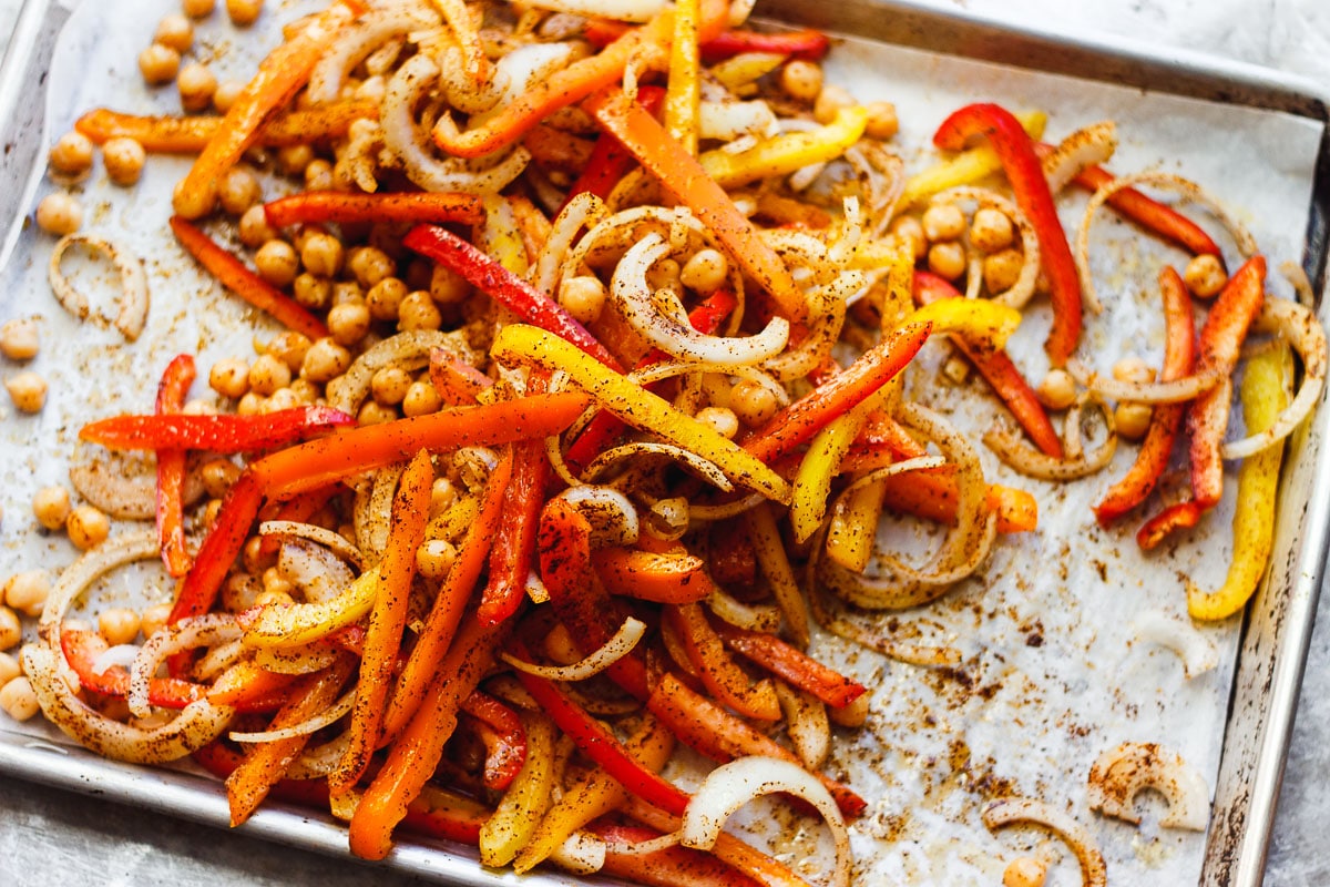 Roasted sliced bell peppers and onions on a sheet pan with browned edges and a light coating of spices