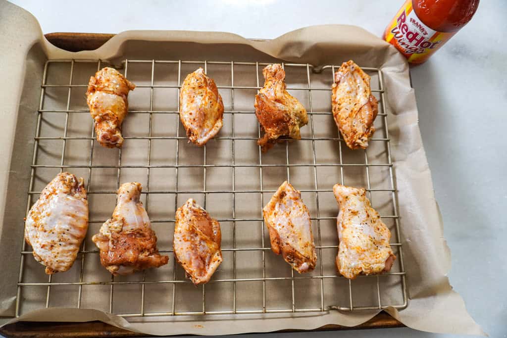 Seasoned chicken wings arranged in a single layer with space between each piece on a wire rack set over a sheet pan