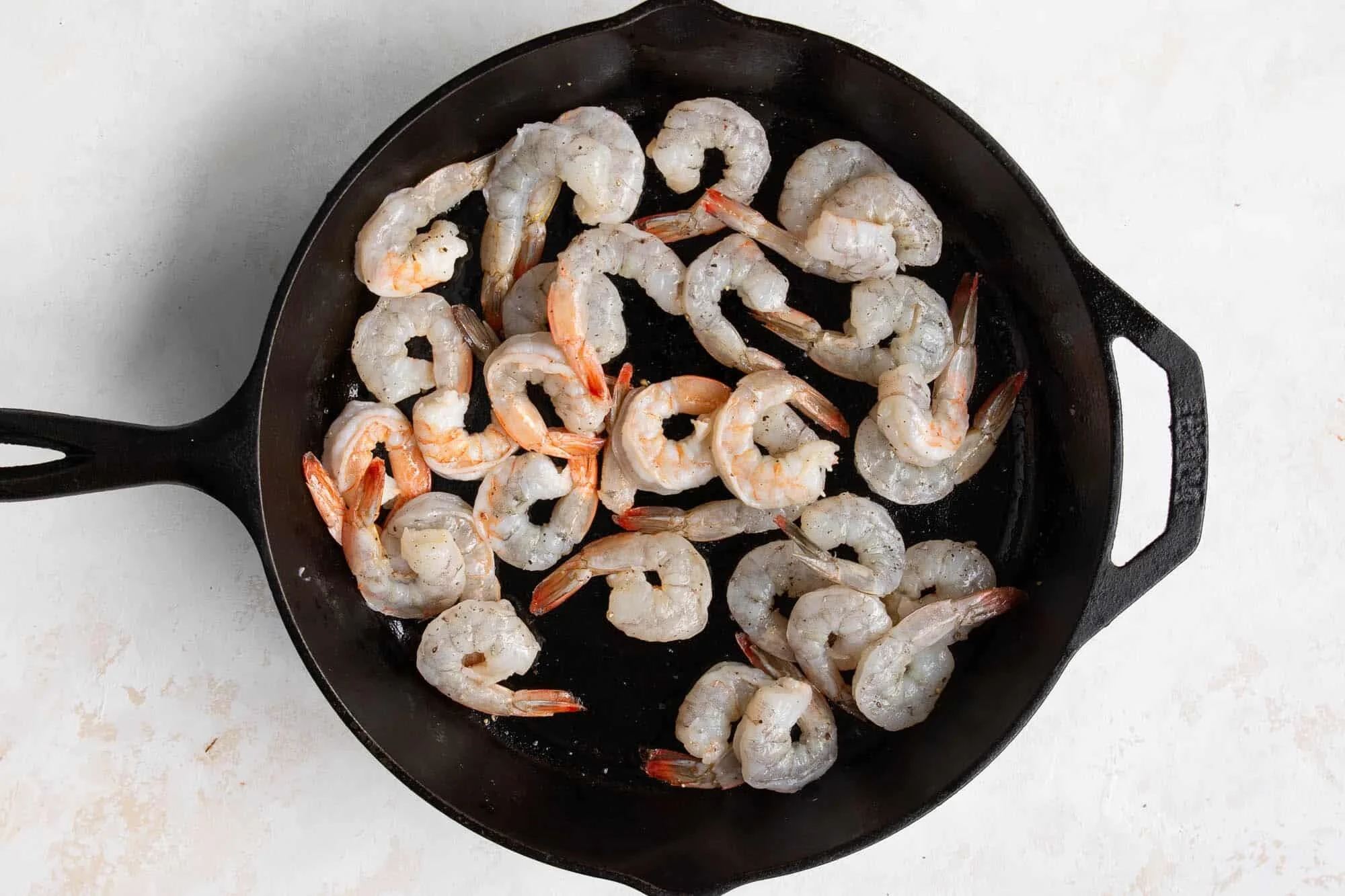 Shrimp searing in a hot skillet with light browning on the edges and steam rising